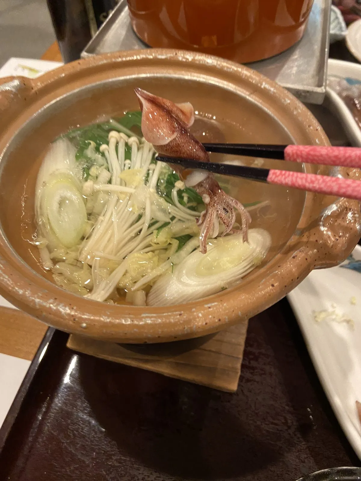 Firefly squid held in chopsticks over a small shabu-shabu pot
