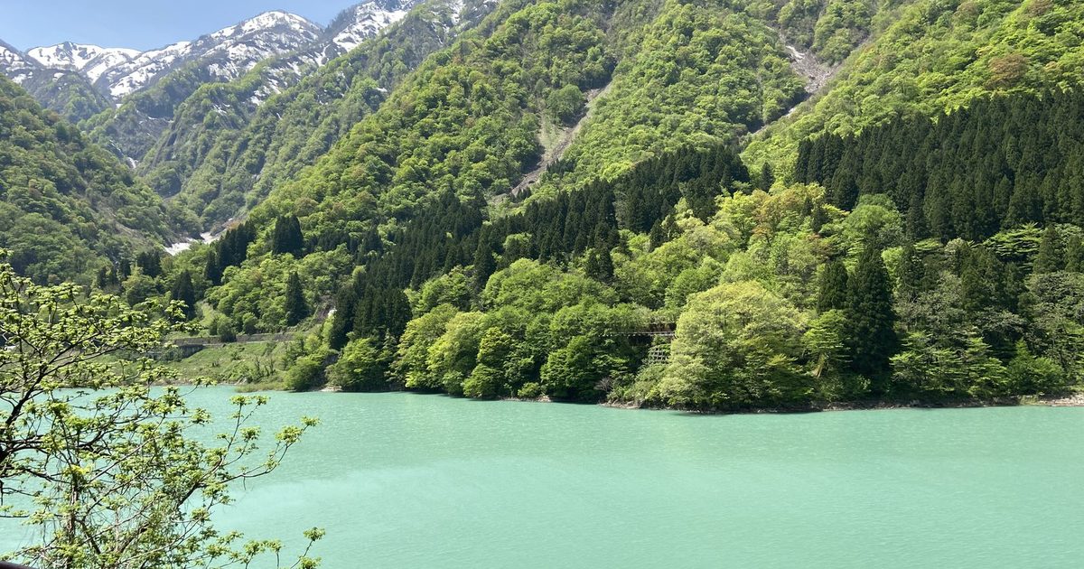 Emerald green dam lake and snow-streaked mountains seen from the Kurobe Gorge Railway